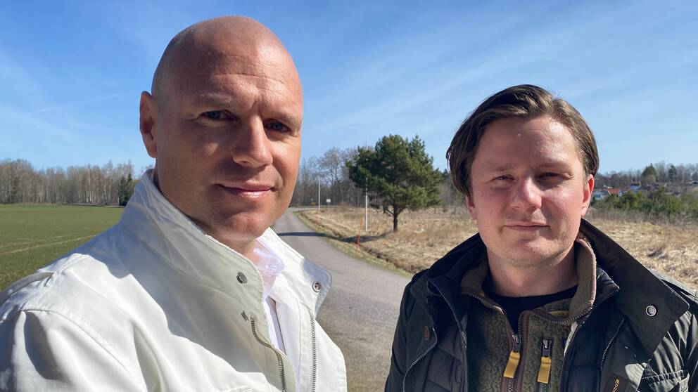 Fastighetsutvecklarna Niklas Johansson och Alexander Lundvall står vid en väg och en golfbana under en solig dag.