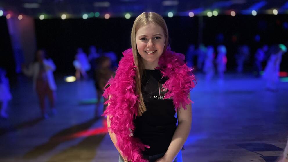 Tjej med långt blont hår står med med rosa boa runt halsen.