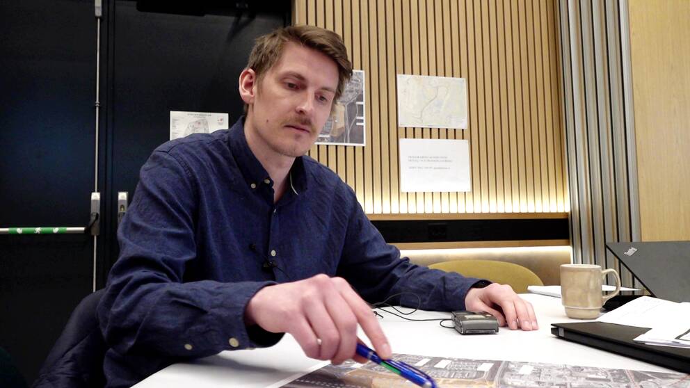 Planarkitekten Samuel Falk sitter vid ett bord och pekar med en penna på en karta.