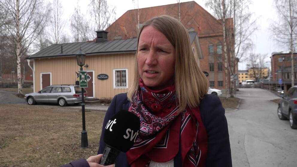Kvinna i sjal som står på en gata och framför henne hålls en mikrofon upp.