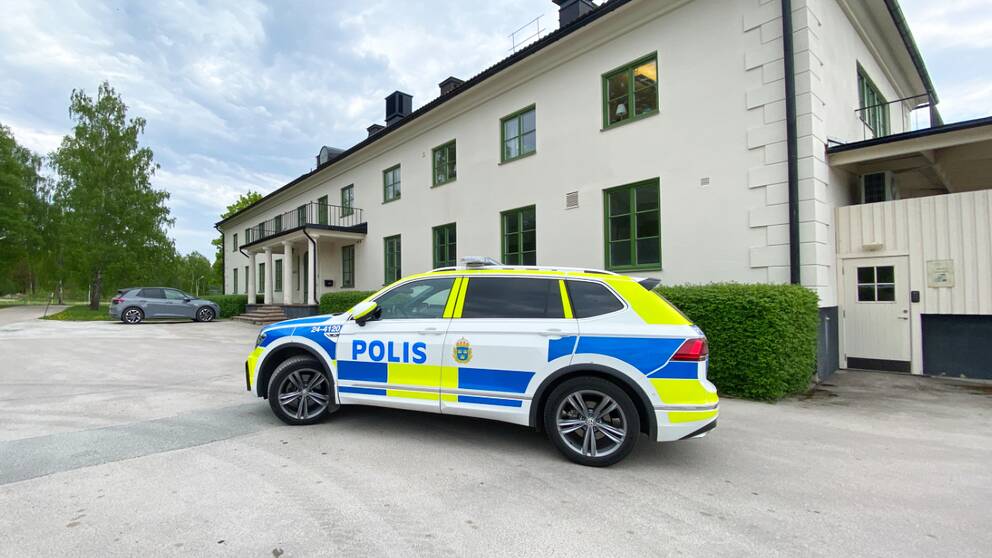 Polisbil står parkerad utanför en vit, äldre byggnad, där det drivs ett sis-hem.