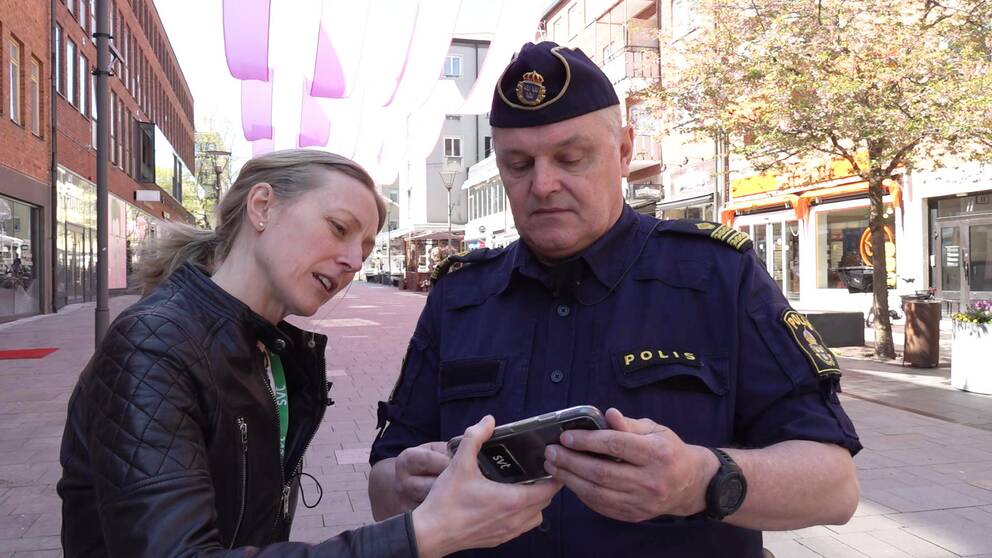 Kvinnlig reporter på SVT visar telefon för manlig polis i centrala Västerås.