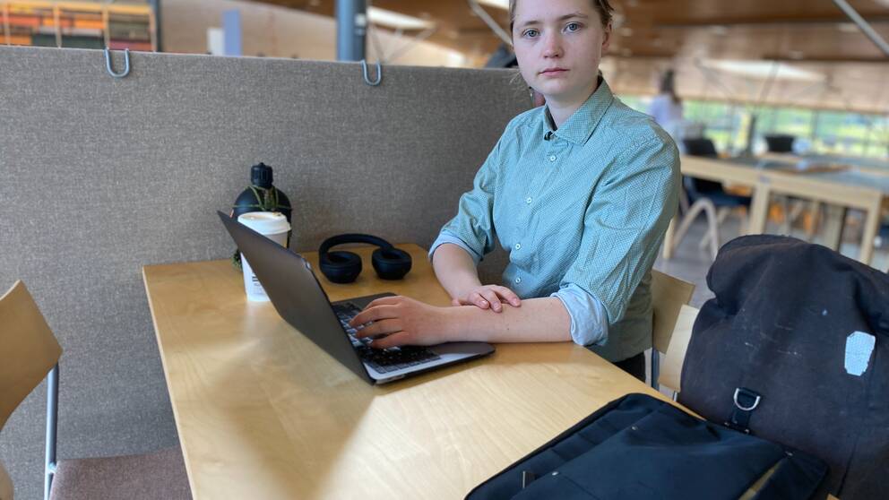 En bild på en student, James Jonsson, i en grönblå skjorta som sitter framför en dator.