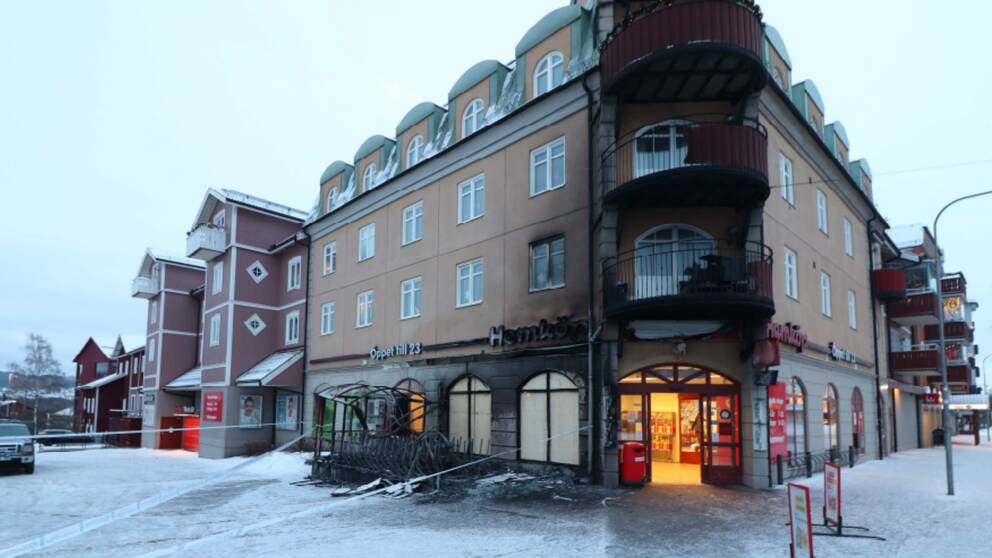 Mörk sot ligger över tre balkonger - nedanför ser man att entrén till matvaruaffären är alldeles svidd och att utrymmet där kundvagnar parkeras är nedbränt.
