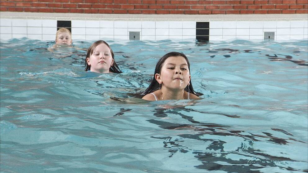 En bild på tre barn som simmar i en pool.