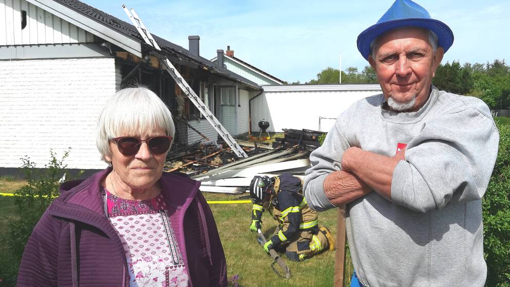 Två personer står framför ett hus som har brunnit.