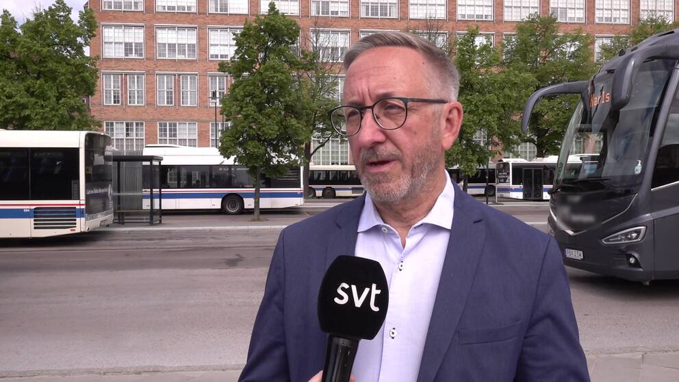 Man klädd i kaval och vit skjorta står framför centralstationen i Västerås med bussar i bakgrunden