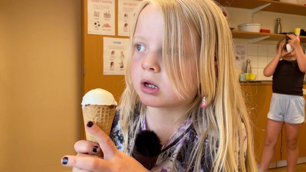 Signe Persson sitter med en glasstrut i handen och tittar ut genom ett fönster.