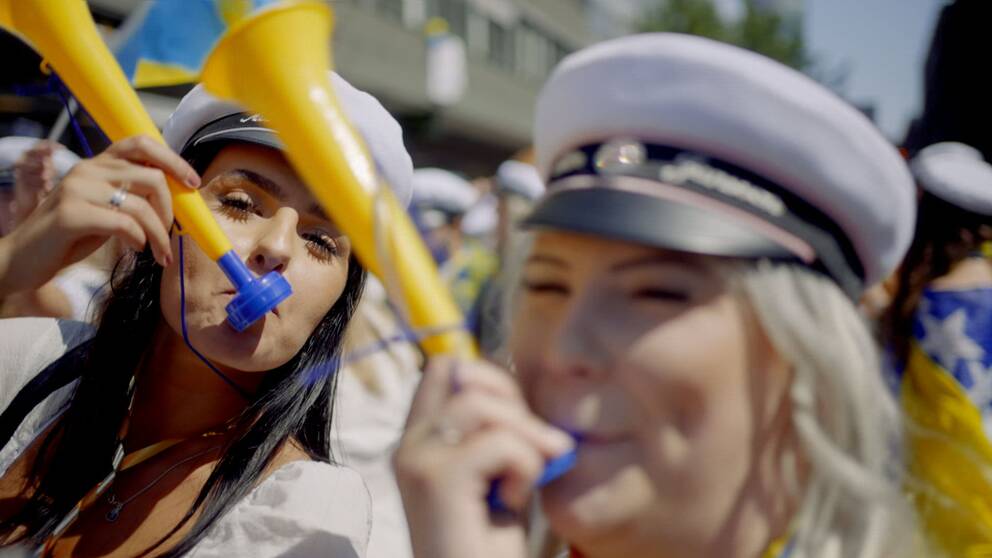 Två unga kvinnor med studentmössor blåser i gula och blå trumpeter i Västerås.