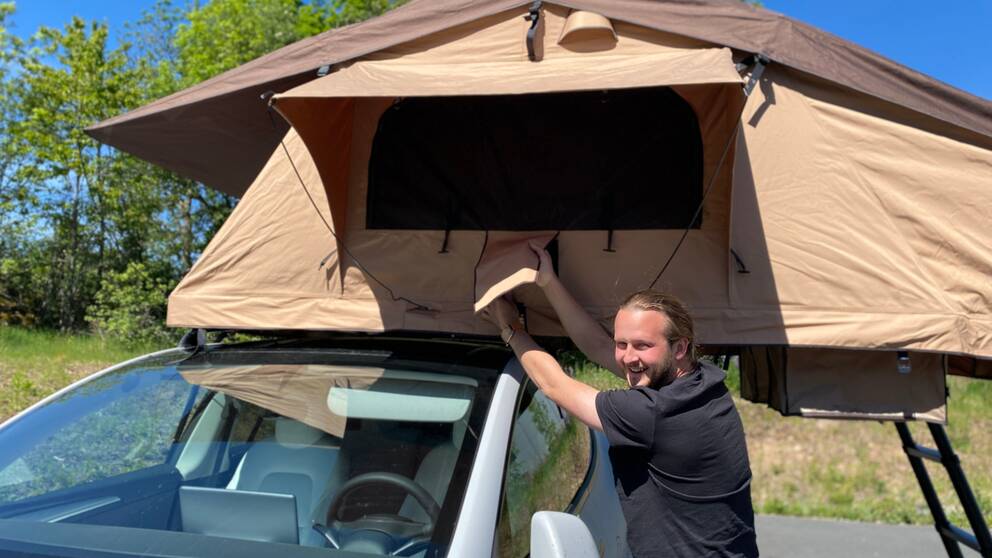 En man står framför en bil som har ett tält på taket.