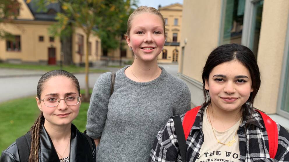 Tre unga tjejer: Shahed Shakweh, Carolina Horn-Berlin och Rand Naia, fotograferade utomhus framför gula byggnader.