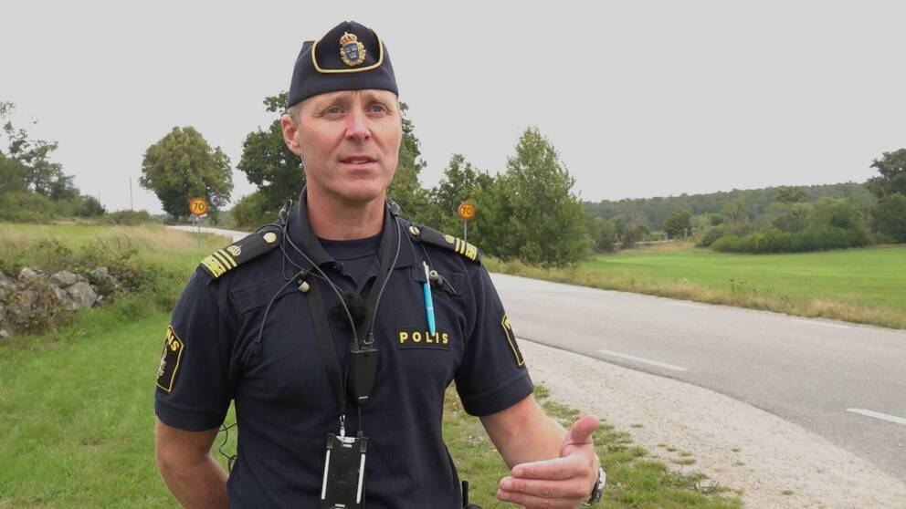 Manlig polis i uniform och med polismössa står intill en 70-väg och tittar snett till höger i bild. Petter Wahllöf, trafikpolis, Karlskrona. Silletorpsvägen, Allatorp, Rosenholm.