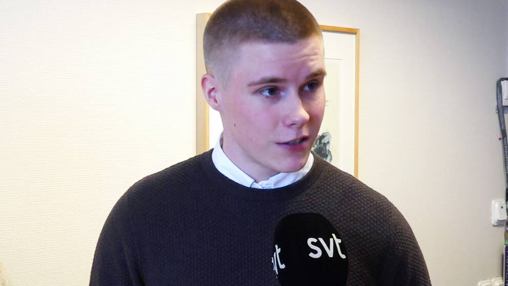 en korthårigman står i en brun tröja framför en vit vägg.