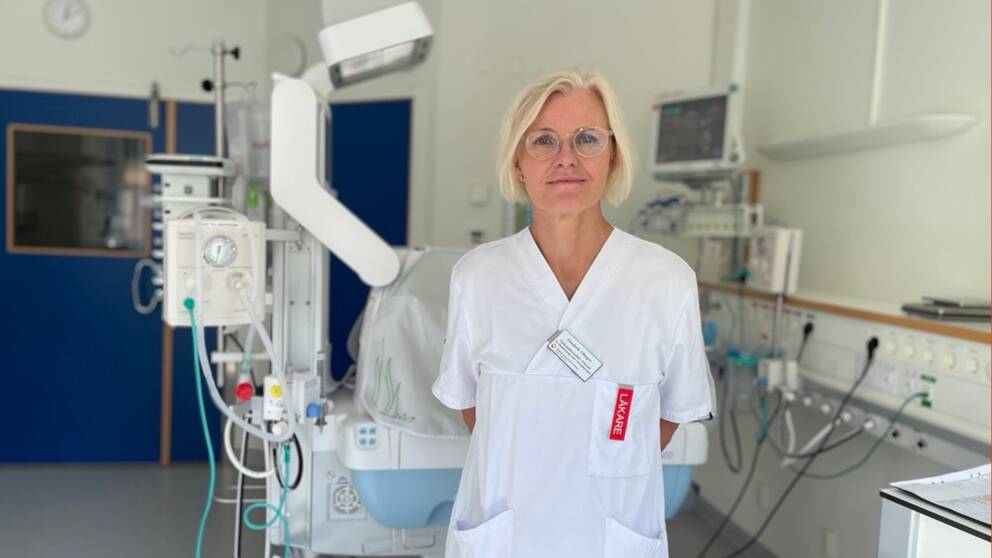 Elisabeth Olhager står i läkaruniform framför en kuvös och tittar in i kameran.