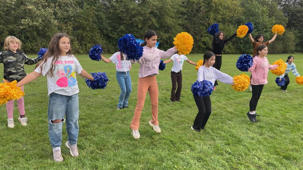 Elever hoppar som cheerleaders på gräsmatta