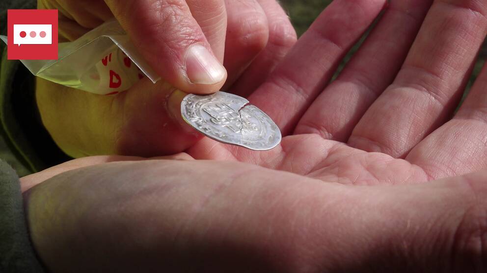 På bild syns ett gammalt silvermynt, en hand och några fingrar.