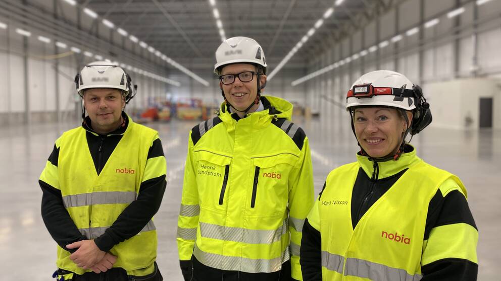 Tre personer i varselväst ler i Nobias nya fabrikslokaler på Torsvik i Jönköping.