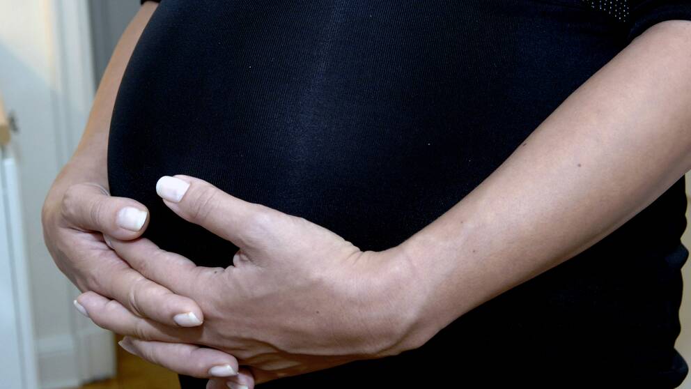 Gravid kvinna håller händerna på magen