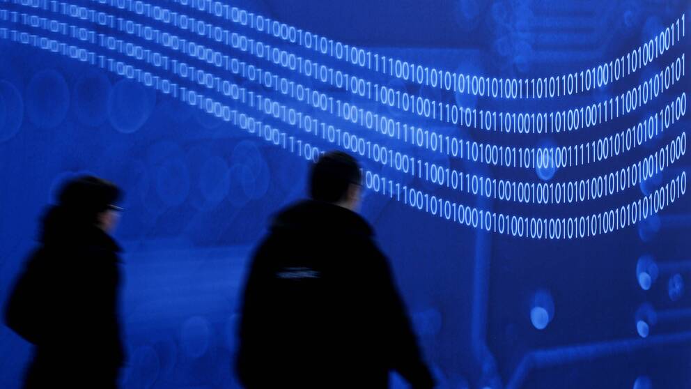 Workers pass a huge video screen with binary code, during last preparations at the Hanover Tech Fair CeBIT, 2012.