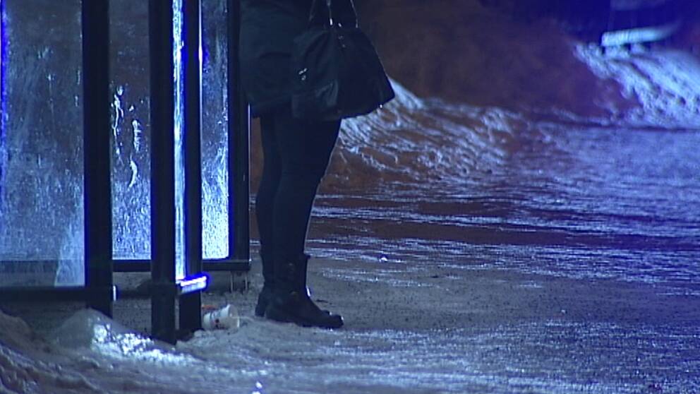 Kvinna väntar vid busshållplats nattetid