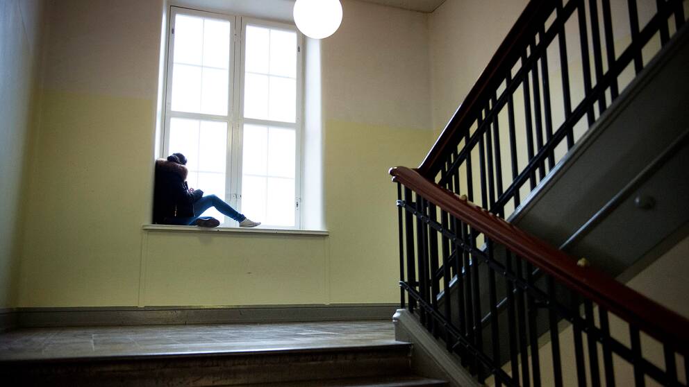 En högstadieelev sitter i ett fönster i en trappa.