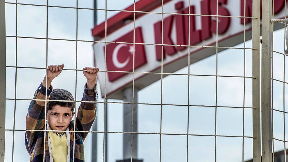 En pojke hänger på stängslet vid gränsen mellan Syrien och Turkiet.