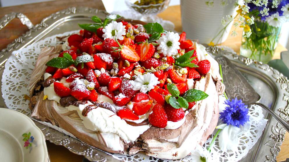 fin tårta med jordgubbar och blommor på maränbotten på gammaldags bricka.