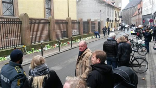 Här vid Synagogan i Krystade, strax söder om Nørrebro station fortsätter människor att placera blommor. Trots att det är mycket folk här så är det väldigt tyst. Det är tydligt att man är tagen av det som hänt.