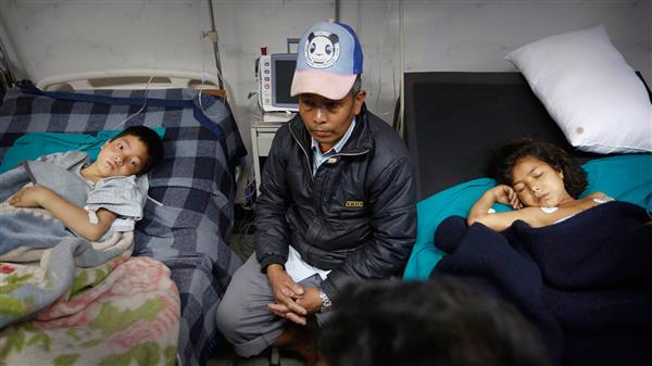 En man sitter bredvid sina skadade barn i ett sjukhus i Katmandu. Foto: TT