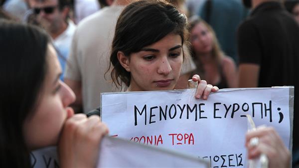 En ung kvinna håller upp en banner med texten "Ska vi stanna i euron?" under en demonstration i centrala Aten. Foto: TT