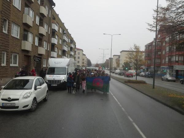 Upp emot 100 personer går i tåget, som nu blockerar trafik på Nobelvägen. Polis beodrar folk in på trottoaren.