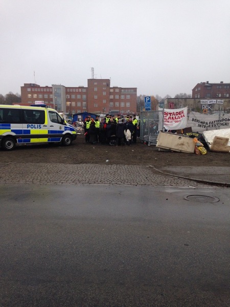 Press är nu tillåtna att passera genom avspärrningarna. Vid ingången till lägret står boende och polis.