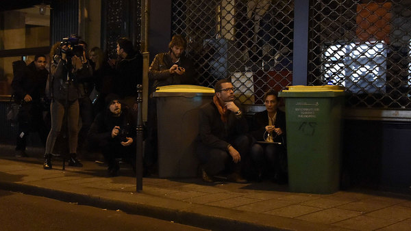 Även journalister tar skydd bakom soptunnor i närheten av Bataclan, konsertlokalen där ett gisslandrama pågår. Foto: TT