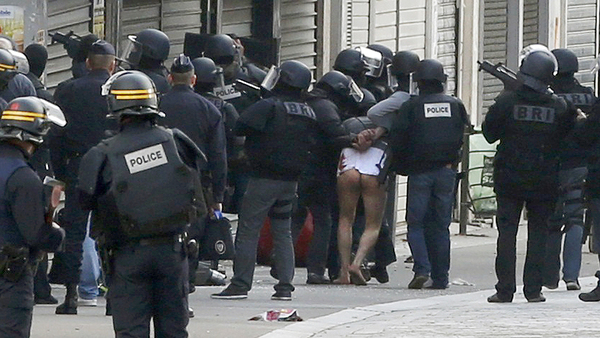 En man i vit tröja och utan byxor grips av polis i Saint-Denis. Foto: AFP/TT.