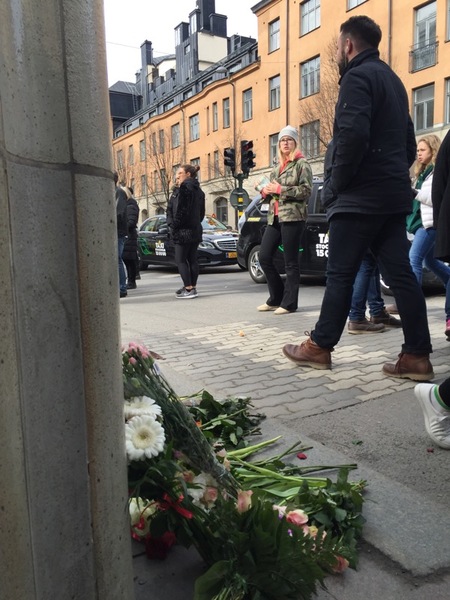 Överallt syns människor med blommor i sina händer röra sig mot avspärrningarna. Här ytterligare en blomsterhög som bildats i korsningen Drottningsgatan /Olof Palmes gata.