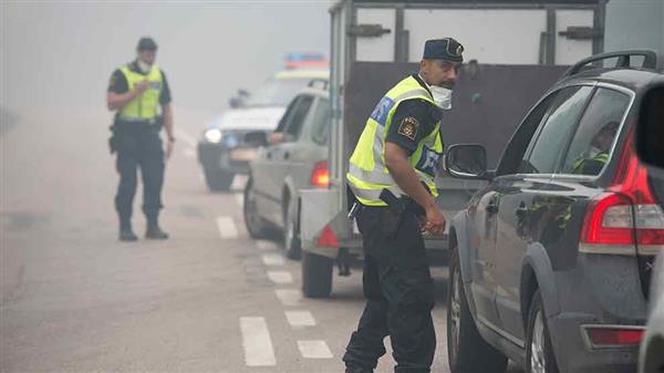 Polis hindrar människor från att ta väg 256 syd om Norberg. Någon knapp mil längre fram finns en av brandens fronter i skogarna syd öst om Norberg och i trakten av Ängelsberg.  Foto: TT